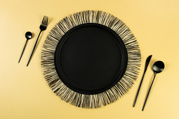 Top view of black wicker table mat, black cutlery on yellow background. Straw round tray, flat lay, copy space. 