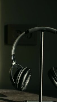 Person hand carefully placing pair of black over ear headphones on dedicated stand, creating an organized, tidy music listening, gaming setup in a dimly lit room. Hanging headphones on stand. Vertical