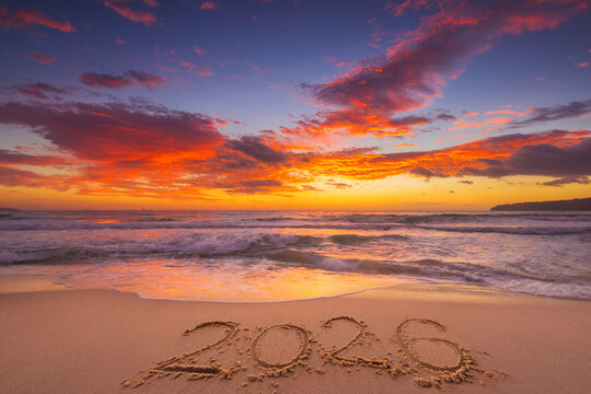Fototapeta Happy New Year 2026 tropical island, beautiful sunrise over the beach and sea horizon with text 2026 handwritten in the sand