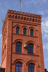 A decaying corner of an abandoned historic red brick factory, featuring boarded-up windows, overgrown ivy, and a modern street lamp contrasting with the ruin