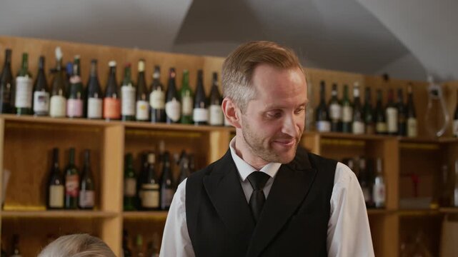 Tilt up shot of professional middle-aged Caucasian sommelier in classic outfit answering questions of participants during wine workshop in luxury restaurant
