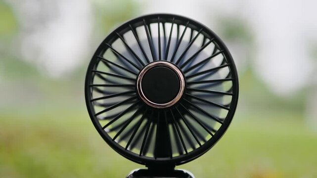 Mini fan black, battery-operated, portable on dry leaves on the ground.