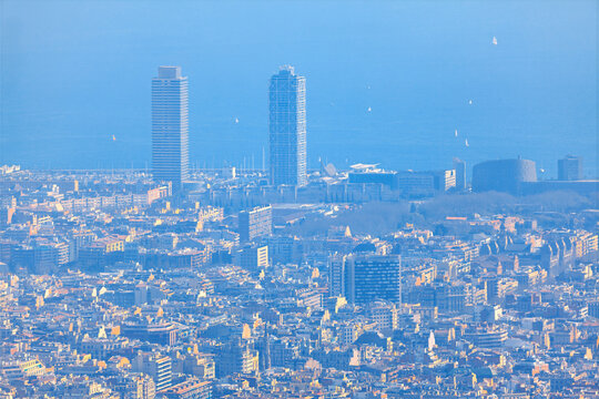 Aerial view of the Barcelona cityscape, showing the dense urban fabric leading towards hazy Mediterranean coastline. Dense urban skyline of Barcelona, Spain. Twin towers rising above city buildings - Powered by Adobe