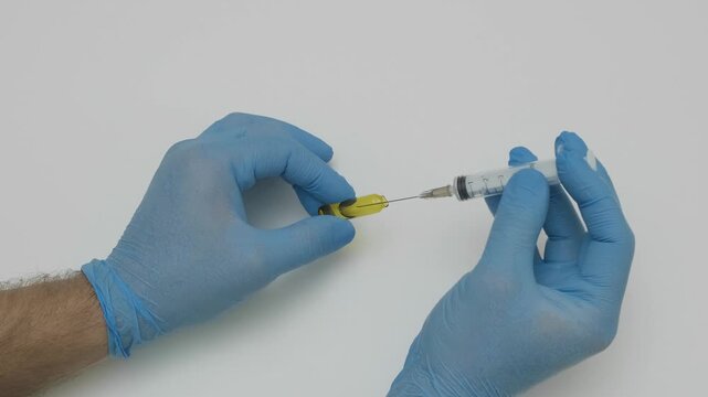 hands in blue gloves collect medicine into a syringe from ampoule slow motion
