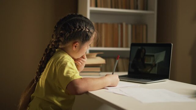 Girl studying at desk with laptop, teacher on screen, writing on paper, braided hair, focused expression, bookshelf nearby, pencil and paper, homework and online learning, remote education at home