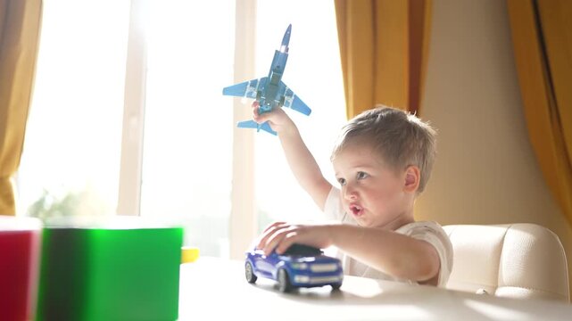 toddler playing with toy car boy at table play near window with sunlight on block and toy car while focused on movement and discovery in indoor setting with colorful cup and toy closeup while boy play