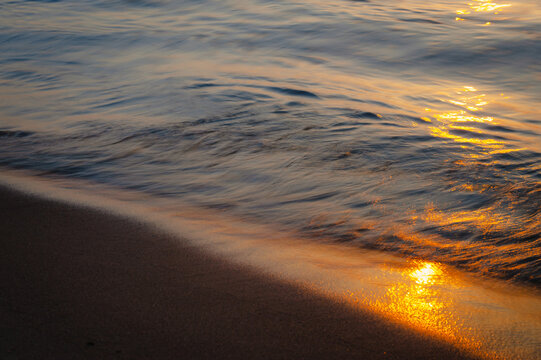 Sea wave washing sandy coastline with smooth long exposure motion, tranquil water texture and minimalistic seascape mood at sunset.