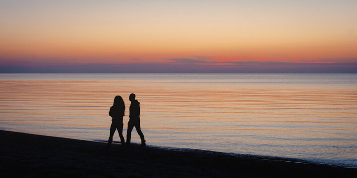 Silhouette couple walking on beach at sunset sea horizon romantic evening. - Powered by Adobe