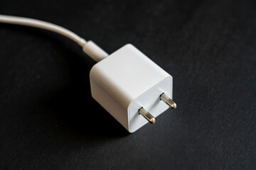 Angled close up photo of a glossy white wall charger adapter (Europlug) with its attached cable on a dark, textured surface, showcasing essential mobile device power accessories and sleek design.