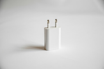 Minimalist product photography of a white rectangular wall charger adapter (Europlug) standing alone on a bright white background, emphasizing simplicity and essential power utility.