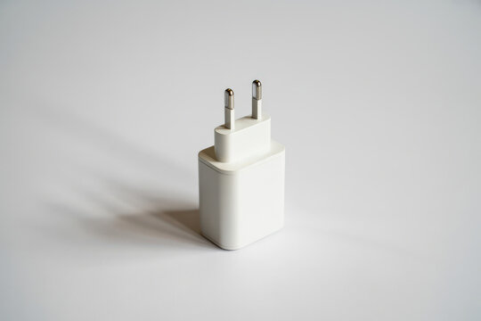 Studio shot of a white rectangular mobile device wall charger adapter (Europlug) standing vertically on a light grey background with soft shadow, focusing on clean product design.