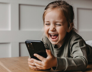 Fototapeta premium Happy child laughing while using smartphone in bright indoor setting