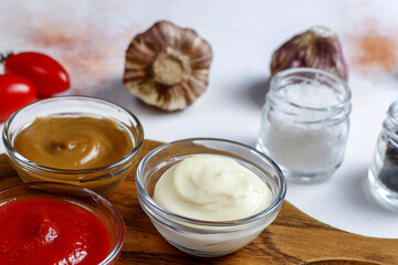 Bowls of Ketchup, Mayonnaise, and Mustard with Salt and Garlic on a Wooden Board