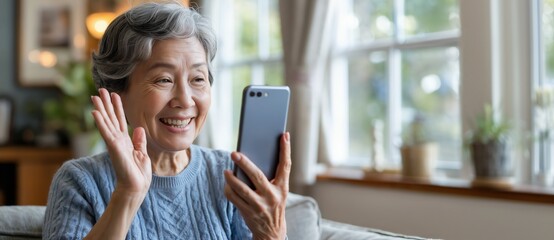 Smiling Senior Woman Waving at Smartphone During Video Call by Window, Digital Communication, Lifestyle Concepts.Mobile Device. Internet Connectivity, Tech Engagement. Useful for Editorial. Copy Space