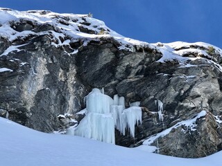 Winter scene showcasing imposing ice formations clinging to rugged rock in the Swiss Alps. The winter landscape is covered in deep snow, creating a dramatic alpine atmoshpere, Kandersteg, Switzerland