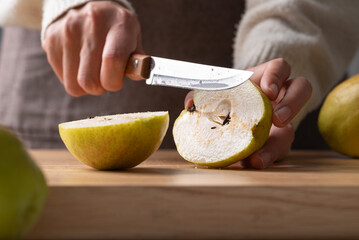 Hand holding kitchen knife and cutting pear on wooden board