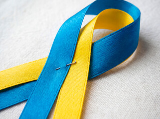 Macro shot of a blue-and-yellow awareness ribbon on a clean white background. Symbol of support, solidarity and hope, representing unity and humanitarian awareness for Ukraine.