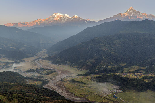 Aerial view of majestic, snow-capped Annapurna mountain range piercing the sky above lush valleys and winding rivers, Astam, Gandaki Province, Nepal.