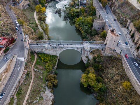 Aerial view of the ancient Puente de San Mart&iacute;n bridge stretching across the Tagus River, connecting the rugged banks with a tapestry of greens and browns, Toledo, Castile-La Mancha, Spain.