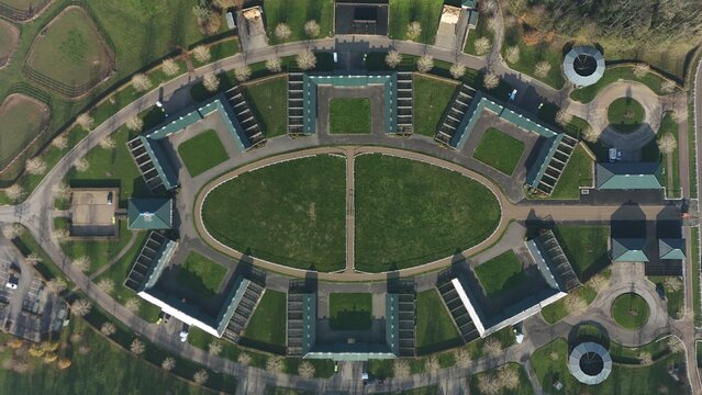 Aerial view of a symmetrical building complex with a central oval lawn and surrounding structures, creating a unique architectural pattern, Newmarket, England, United Kingdom.