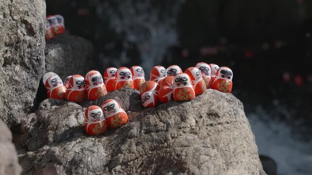 Small red daruma dolls on a stone by a waterall on a sunny day in Katsuoji Temple, Osaka. Japan.
