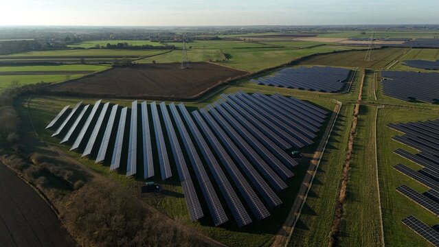 Aerial view of solar panels basking in the soft sunlight against the backdrop of green fields and distant structures, Newmarket, England, United Kingdom.
