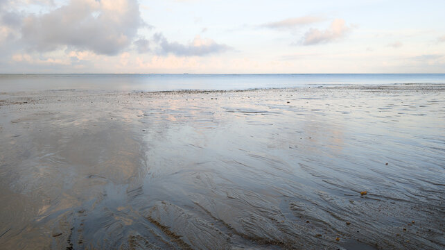 sunset over the sea sandy beach low tide reflections on wet sand under pale sky on ocean water