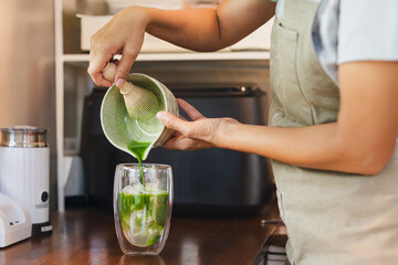 Barista pouring Matcha to a glass of ice with traditional japanese matcha.