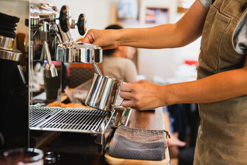 Woman barista steaming jug of milk at coffee machine in a cafe.