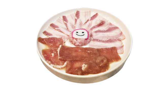 Plate of raw pork belly and loin slices artfully arranged in a fan shape, centered with a cute smiling fish cake decoration