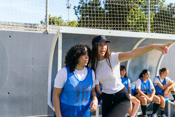 Female coach pointing, instructing young player from the dugout during a soccer game, other team members listening
