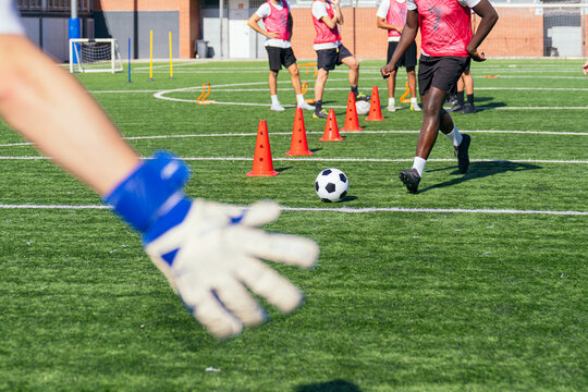 Goalkeeper's outstretched hand reaching towards a soccer ball during intensive football practice with team players