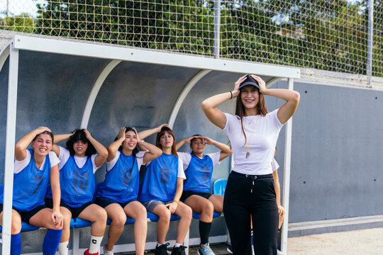 Women's football team and coach posing with hands on heads, celebrating a funny moment on the sidelines
