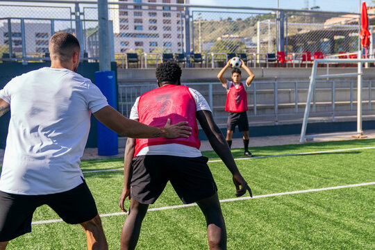 Soccer coach instructing players during a team training session on a green artificial turf field with ball exercises