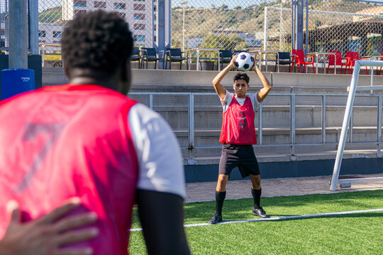 Two male soccer players training on a green pitch. One player holding the ball above his head for a throw in