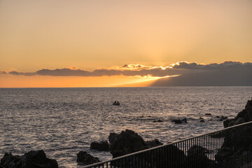 Orange sunset at sea shore promenade in Playa de San Juan, Tenerife, Spain in the south of Tenerife with ocean waves crushing black lava rocks