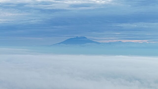 Aerial view of a mountain peak piercing through a sea of clouds, with trees visible below the fog, creating a serene landscape, Klaten Regency, Central Java, indonesia.