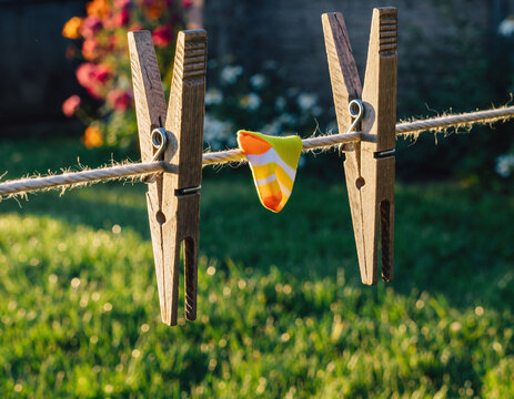 Closeup of a whimsical, colorful sock hanging on a clothesline with wooden clothespins. Evokes feelings of childhood, summer, and simple pleasures. Great for family themes.