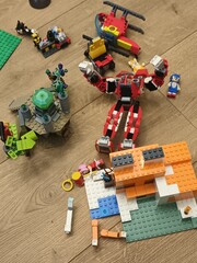 Obraz premium A collection of colorful LEGO creations, including a Marvel superhero mech and a Minecraft-style building, scattered on a wooden floor during playtime