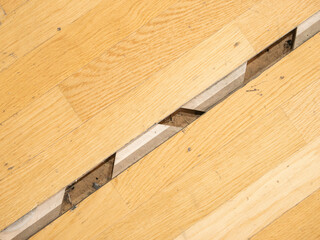 Large gap in playing field parquet of a sports arena due to separated floor locks, needs maintenance