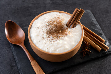 Rice pudding with cinnamon in wooden bowl on black background