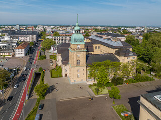 Aerial view of Ludwigskirche's pale stone facade and its verdigris dome dominate the square, framed by the city's rooftops, Darmstadt, Hessen, Germany.