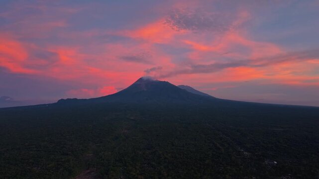 Aerial view of Mount Merapi with its lush green slopes set against a vibrant pink and purple sky, creating a stunning contrast, Klaten Regency, Central Java, indonesia.