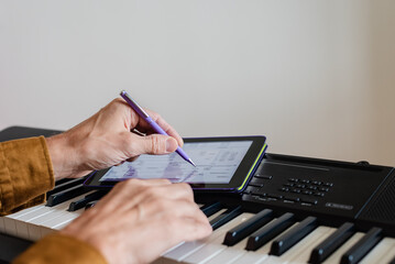 Male pianist using tablet with mobile apps for self study, closeup photo. Using green screen tablet over piano keyboard for digital music concept