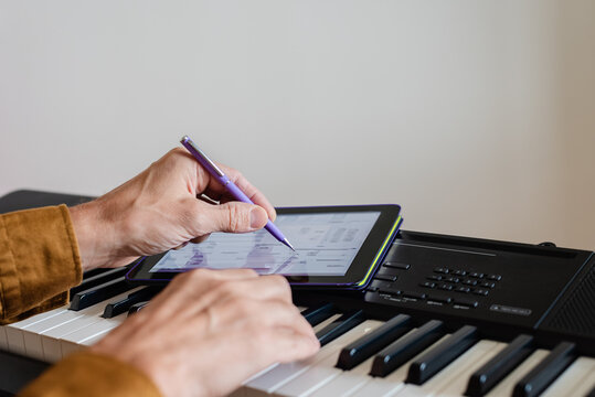 Male pianist using tablet with mobile apps for self study, closeup photo. Using green screen tablet over piano keyboard for digital music concept - Powered by Adobe