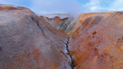 Drone shot over Iceland’s Hverir geothermal fields, revealing dramatic steam vents, colorful sulfur textures, and raw volcanic energy in a surreal otherworldly landscape. - Powered by Adobe