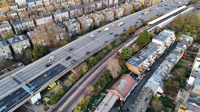 Aerial view of the A40 Westway highway with cars and railway tracks cutting through buildings, showcasing a contrast between transport and residential areas, London, United Kingdom.