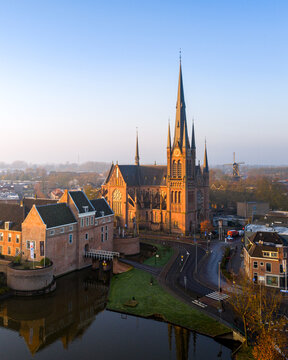 Aerial view of the Sint-Bonaventurakerk's towering spire piercing the sky, juxtaposed against the ancient Kasteel Woerden, a dance of light and shadow, Woerden, Utrecht, Netherlands.