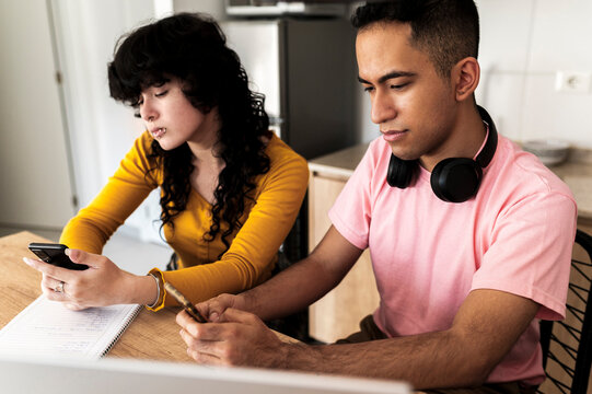 Focused latino friends using smartphones for study references in digital lifestyle