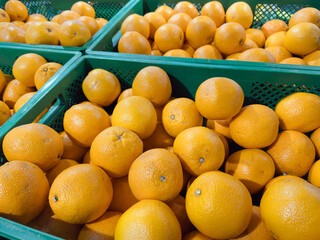 Bright orange oranges piled in green plastic crates at a supermarket produce section, showcasing fresh citrus fruits ready for sale in a grocery store.